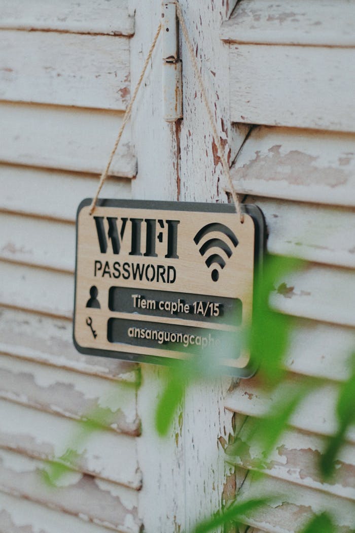 Home A wooden sign displaying WiFi login details on a rustic wall, surrounded by greenery.